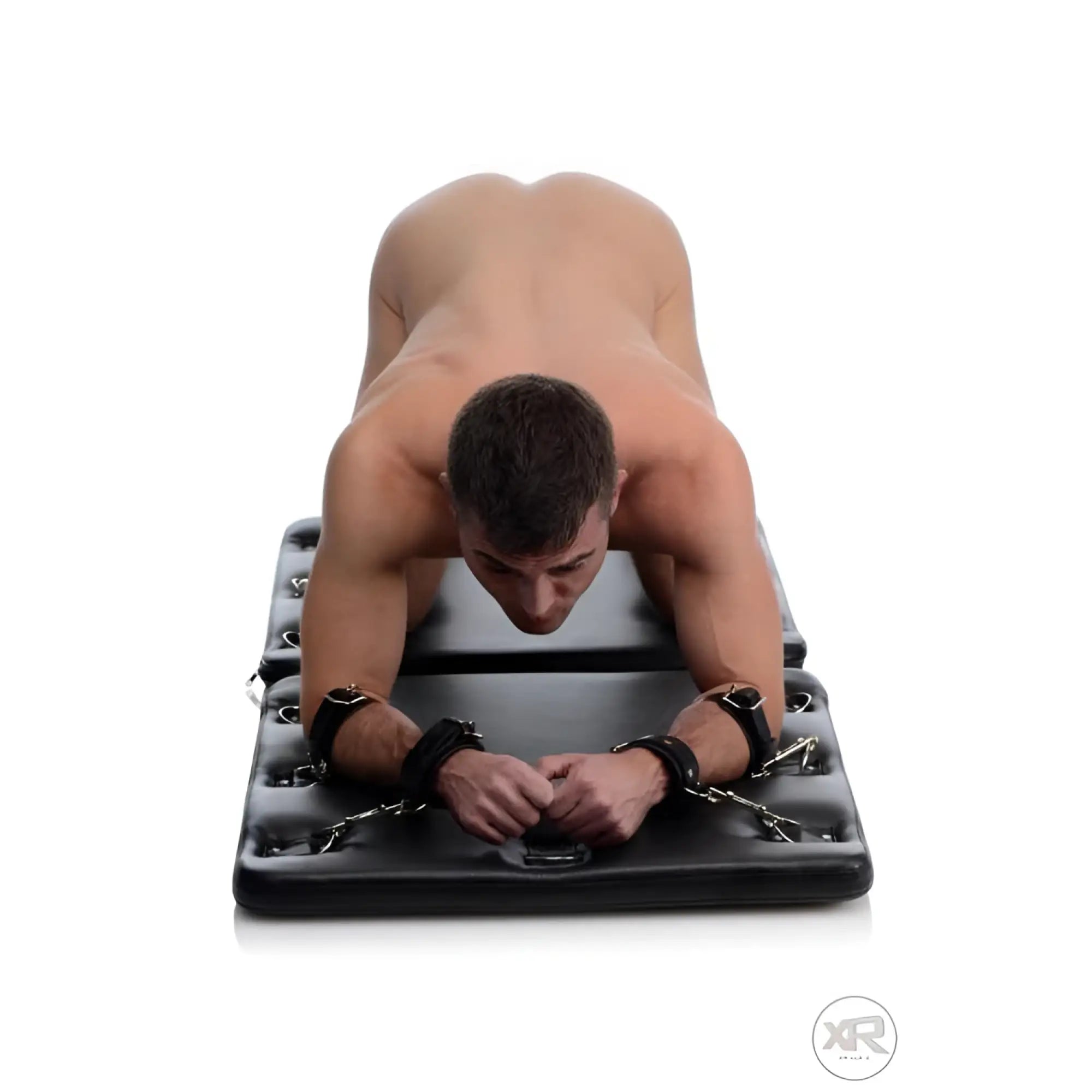 Strict The Bondage Board: A black, padded mat with metal hardware and cuffs securing a man in a prone position.