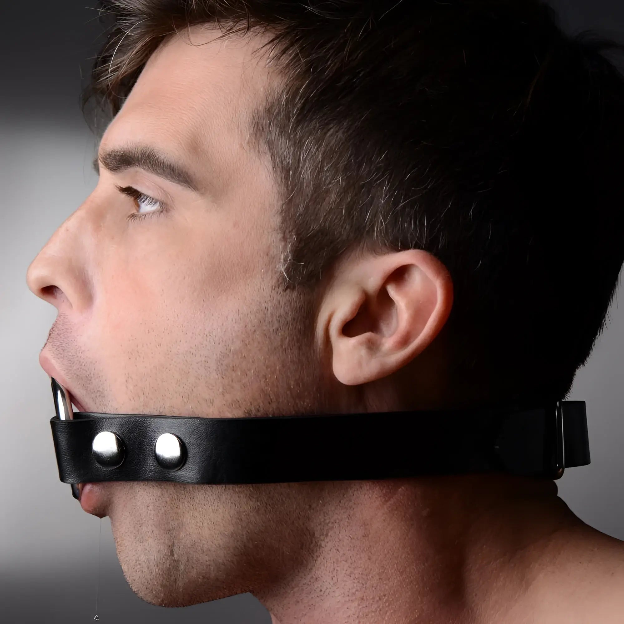 Profile view of a man wearing a black leather Strict The Deep Throat Gag with a silver metal ring.