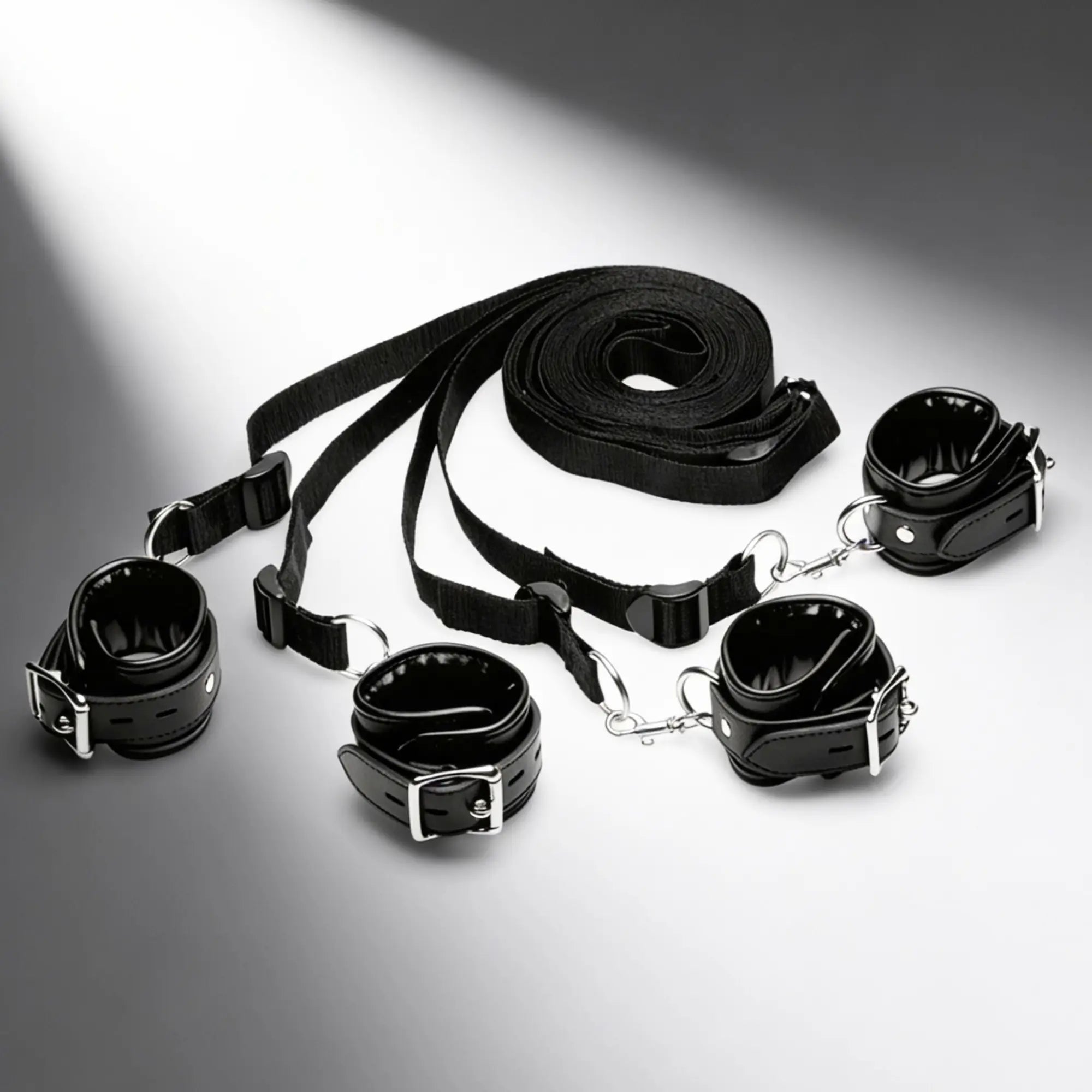 Strict Deluxe Bed Restraint System: Black four-piece adjustable cuff set with silver buckles and connecting nylon straps.