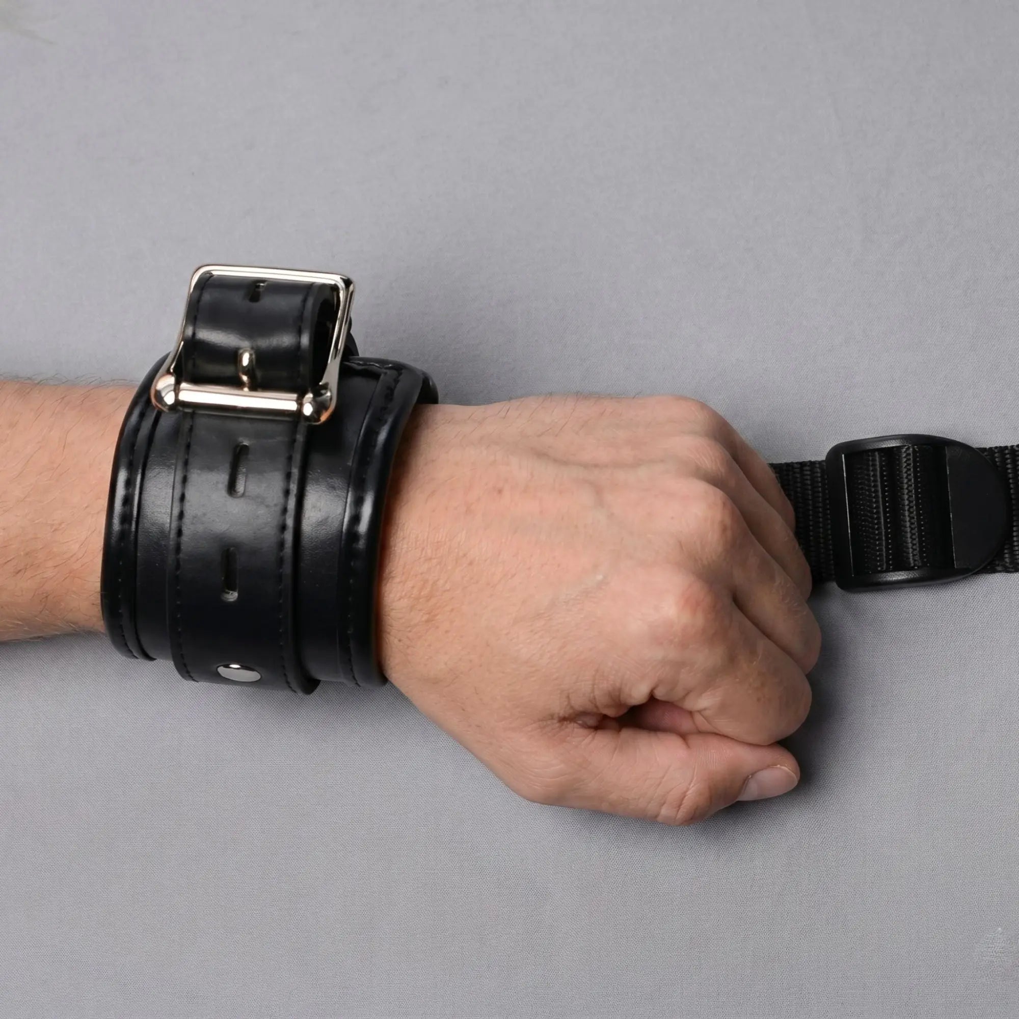Strict Deluxe Bed Restraint System: Black padded faux-leather wrist cuff with silver buckle on a person's wrist.