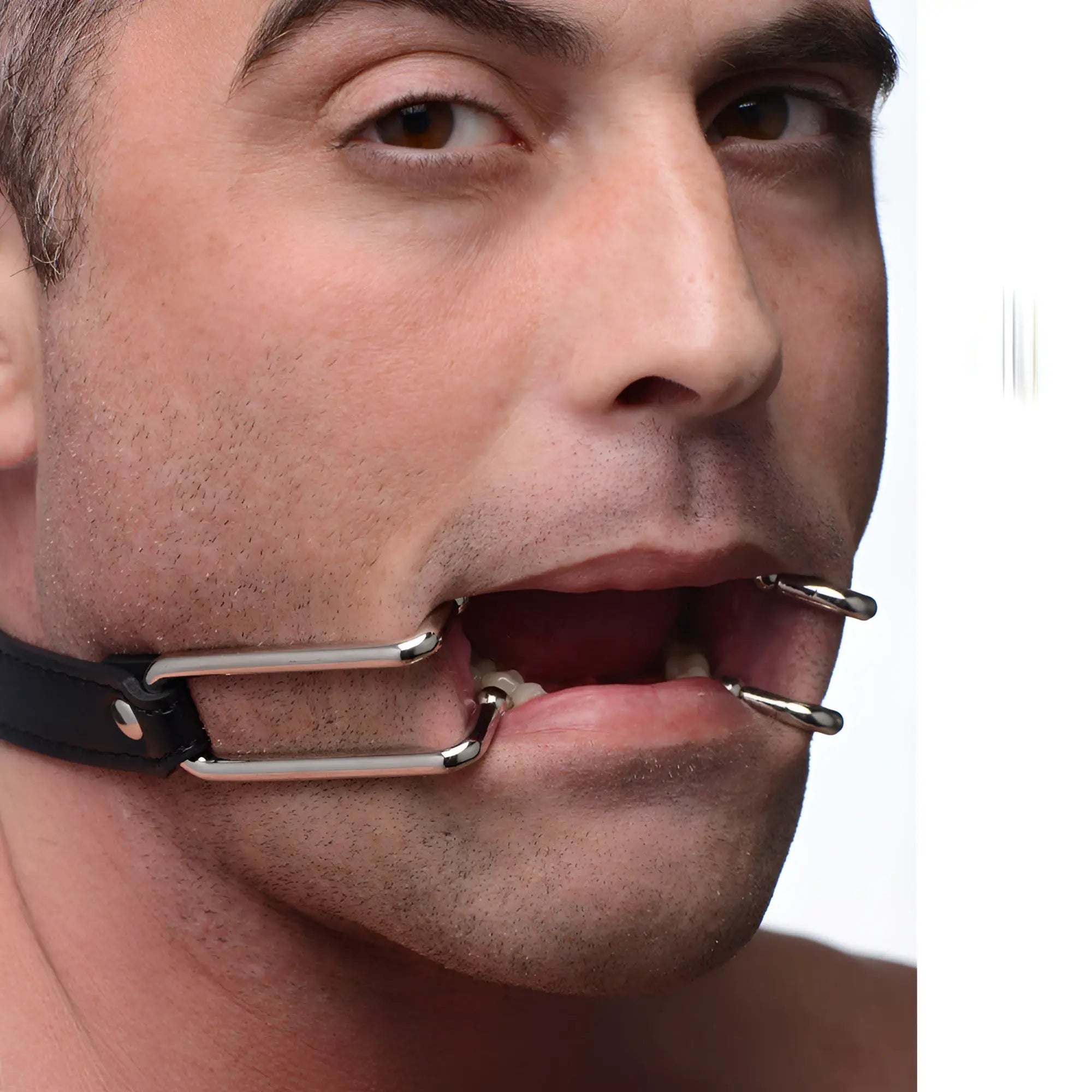 Strict Hook Claw Mouth Spreader: Silver metal hooks attached to a black strap, holding a person's mouth wide open.