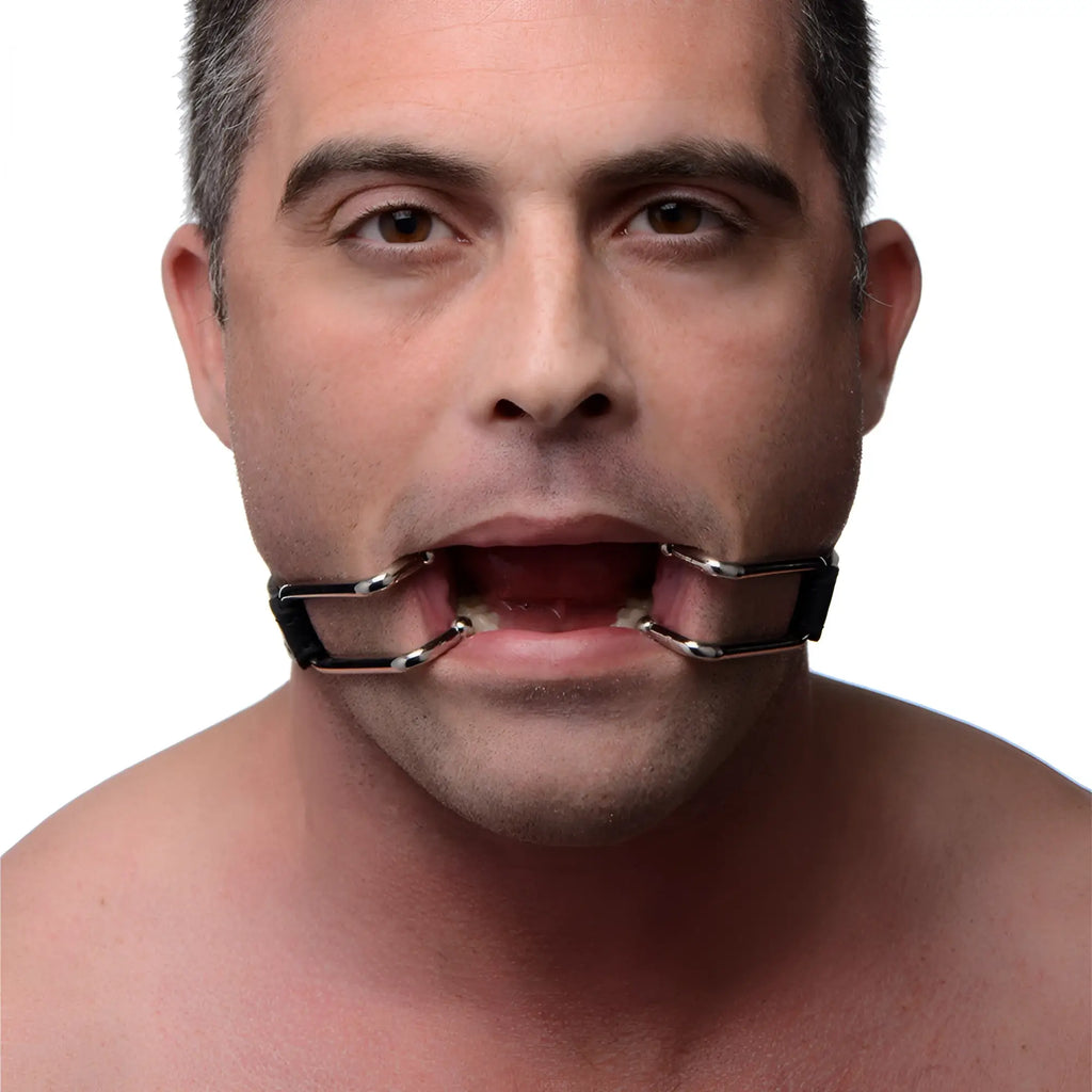 Strict Hook Claw Mouth Spreader: A man wears a chrome-colored, metal-framed jaw opening device against his mouth.