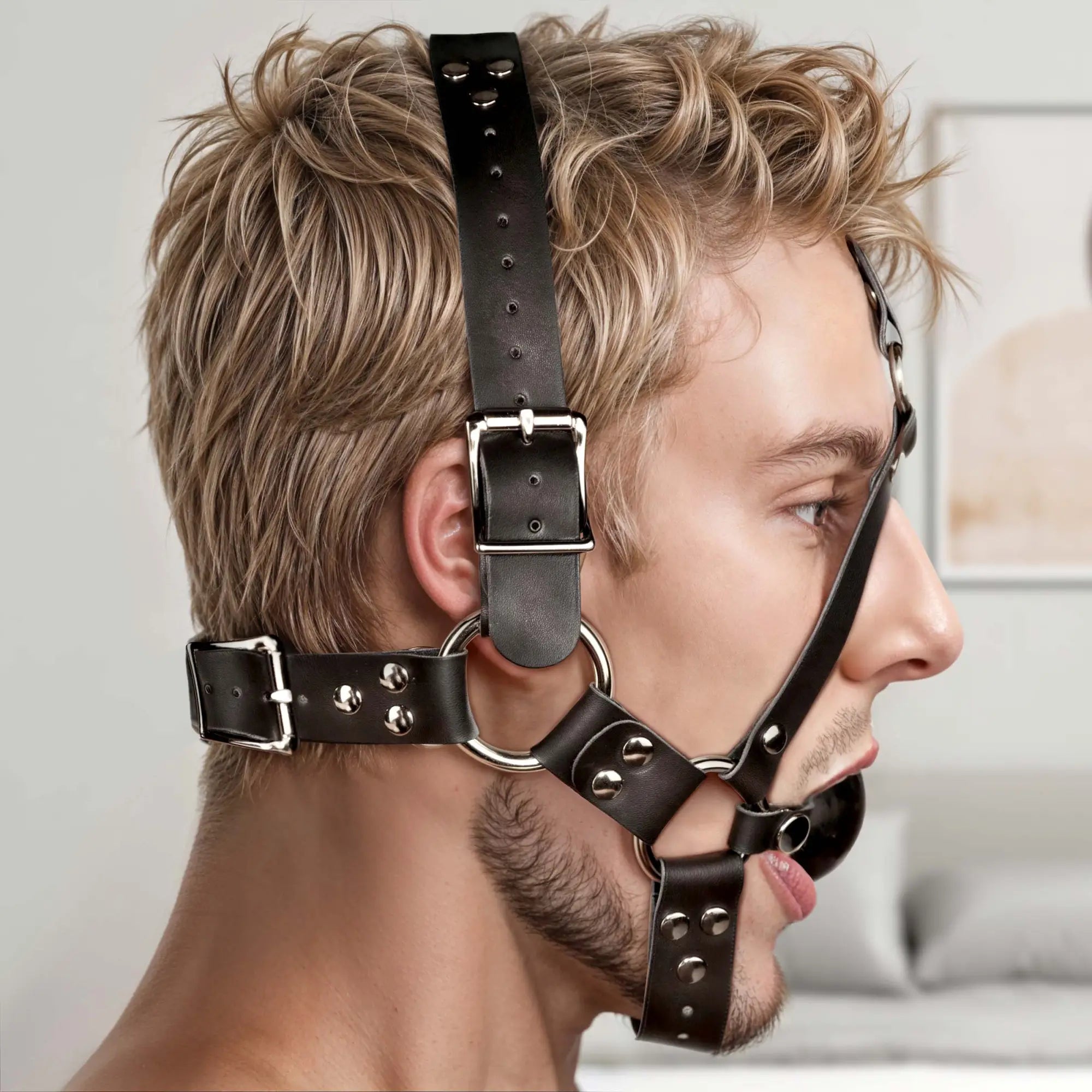 Strict Leather ball gag harness: black leather straps with silver buckles and hardware worn on a man’s head.