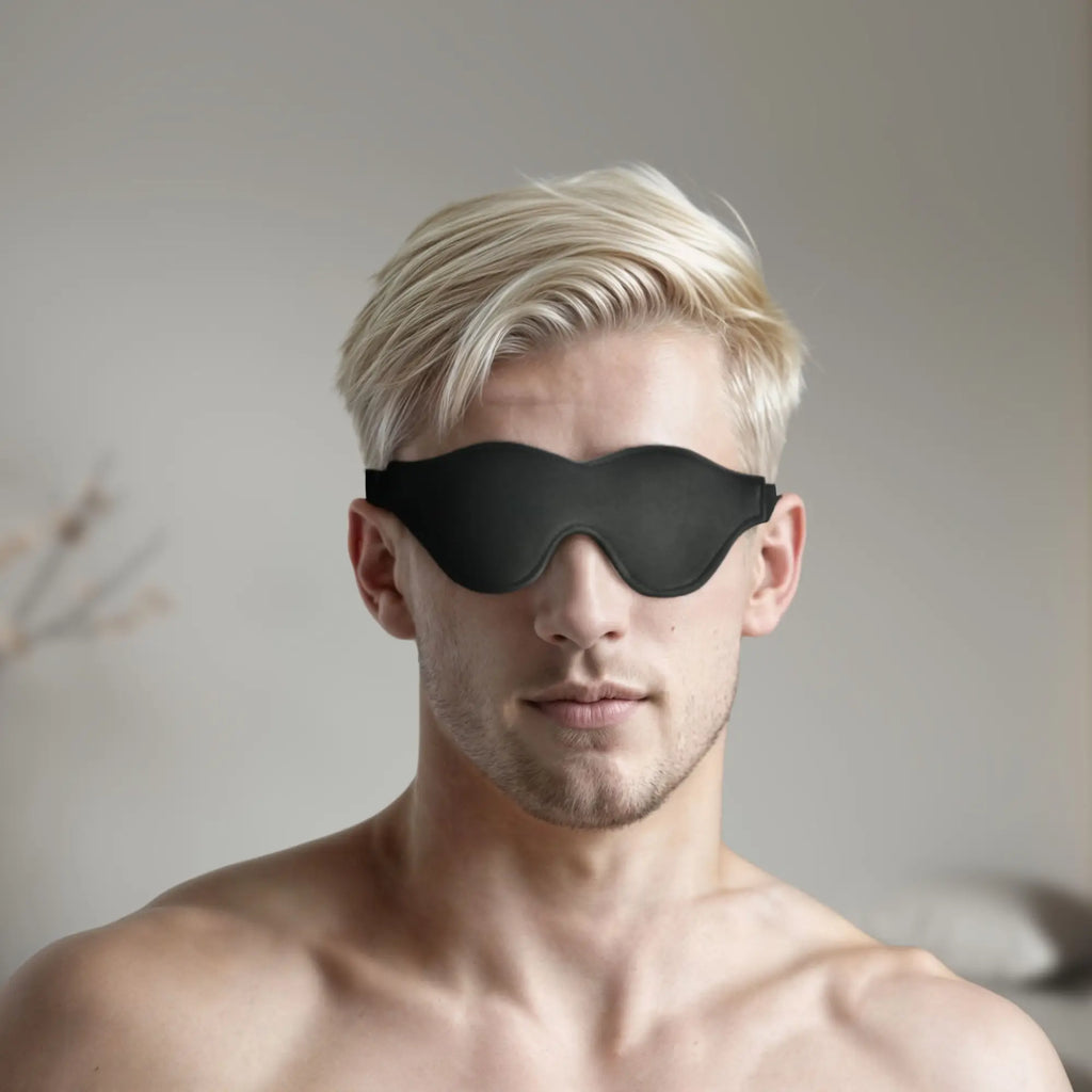Blond man wearing a black, fleece-lined Strict Leather blindfold that covers his eyes.