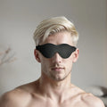 Blond man wearing a black, fleece-lined Strict Leather blindfold that covers his eyes.