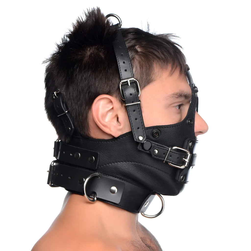 Strict Leather black leather head harness with silver-tone buckles, straps, and a removable gag, worn by a man.