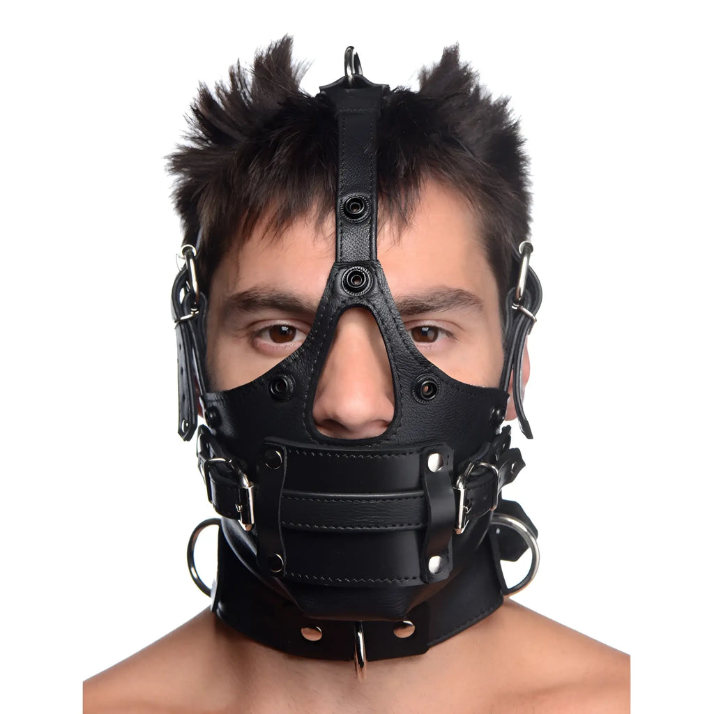 A person wearing a black Strict Leather head harness with a removable gag, featuring buckles and silver hardware.