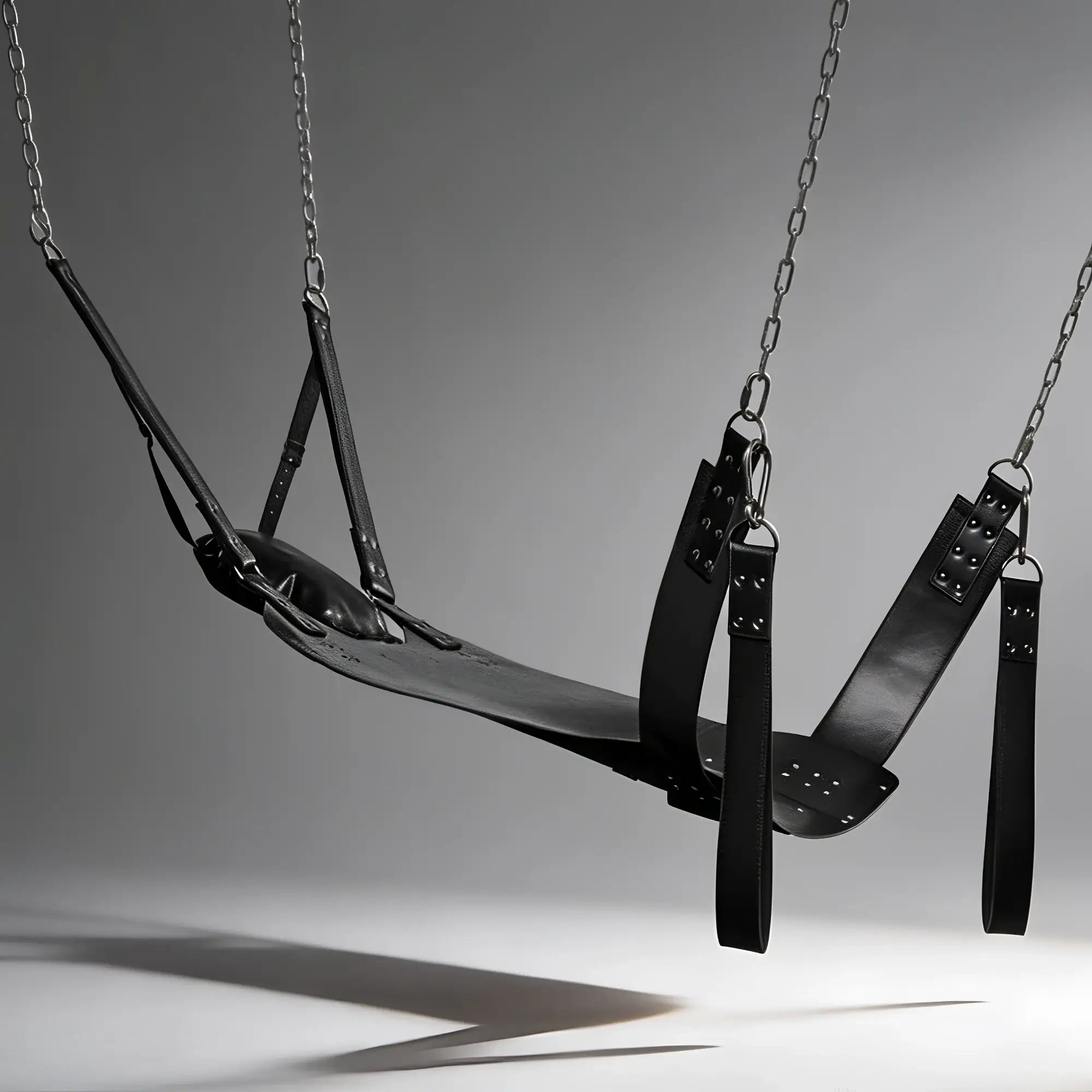 Strict Leather Lined Sling with pillow and stirrups, a black leather hammock suspended by metal chains on a grey background.