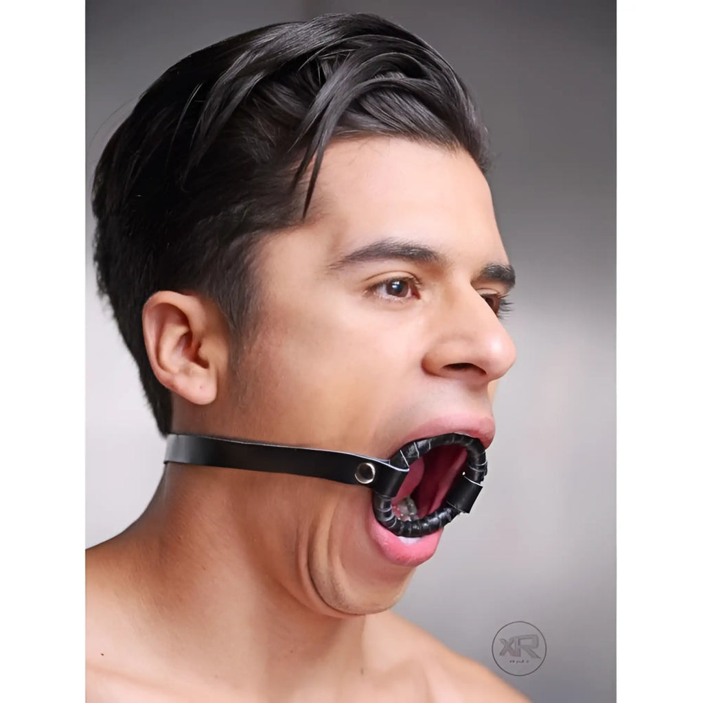 Strict Leather O-ring gag featuring a black leather strap and ring worn by a man in profile against a grey background.