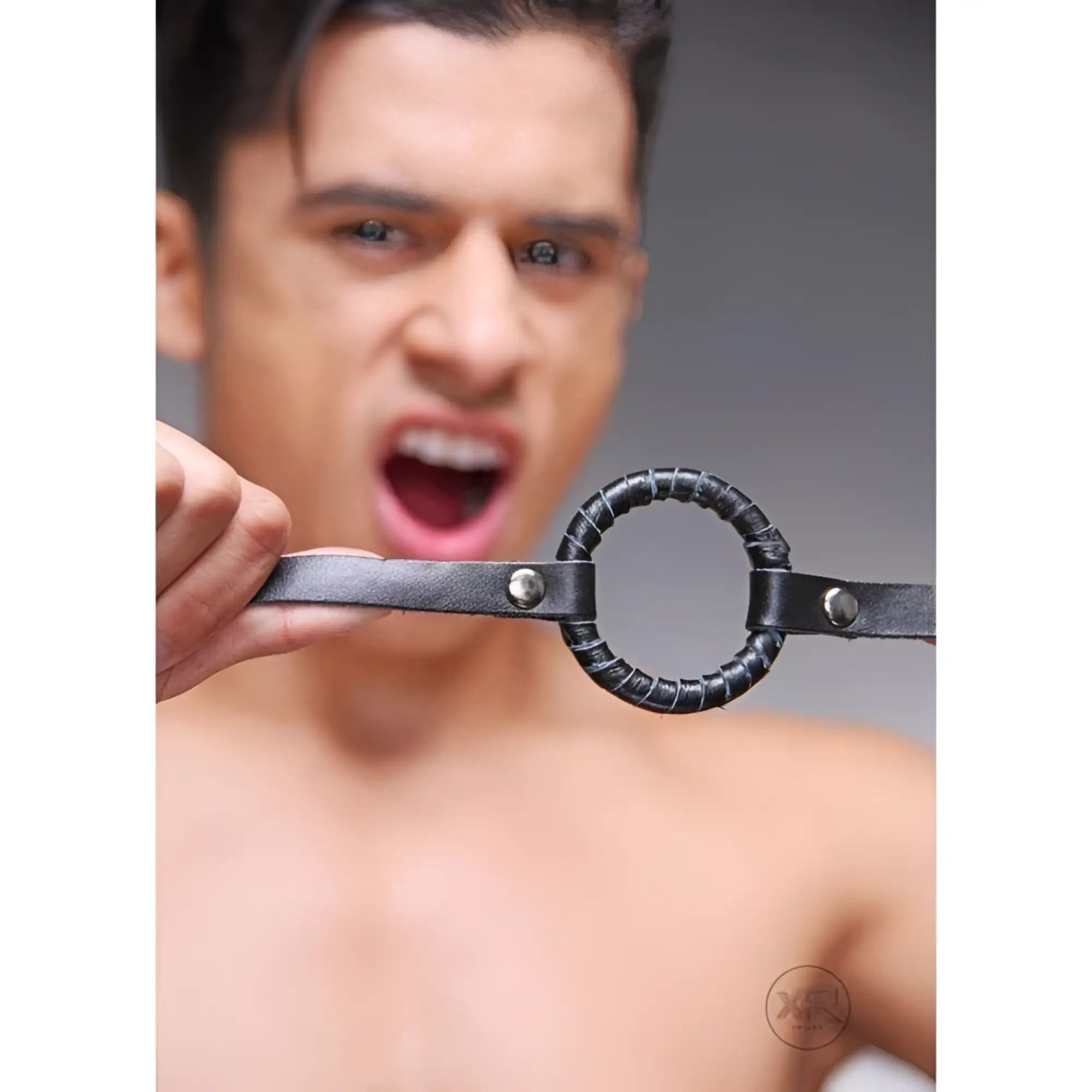 Strict Leather O-Ring Gag: A black leather strap featuring a wrapped circular O-ring held in front of a person’s face.