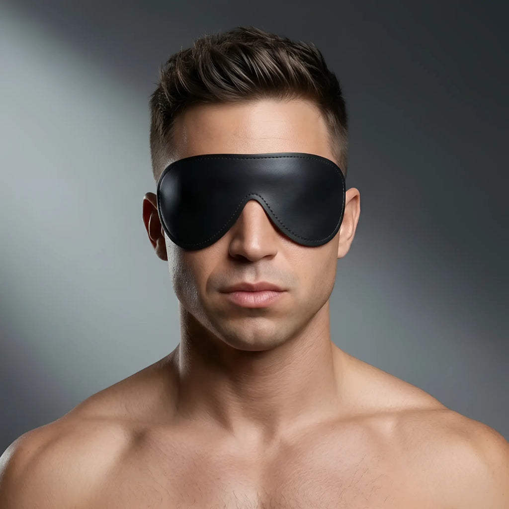 Strict Leather Padded Blindfold: A man wearing a smooth, black leather blindfold against a grey background.