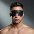 Strict Leather Padded Blindfold: A man wearing a smooth, black leather blindfold against a grey background.