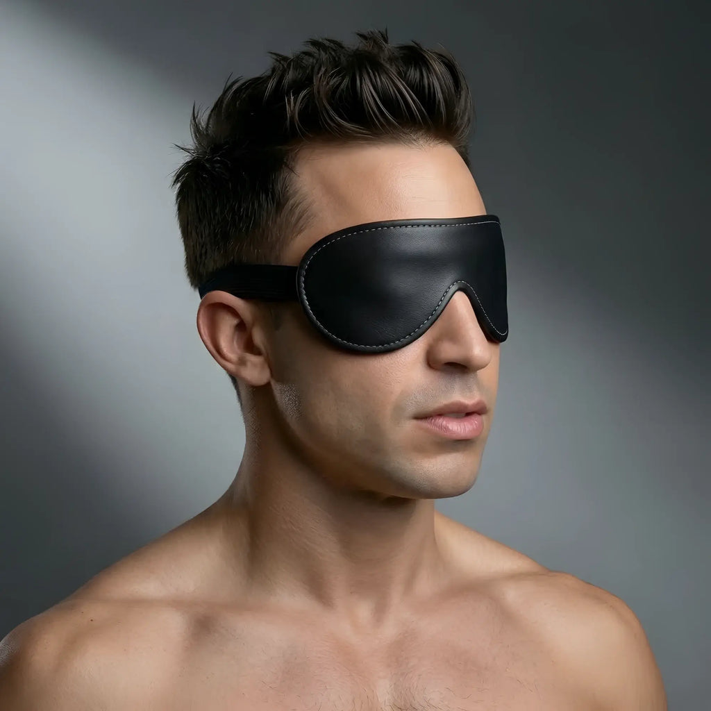 Strict Leather Padded Blindfold: A man wearing a contoured black leather eye mask with white stitching.