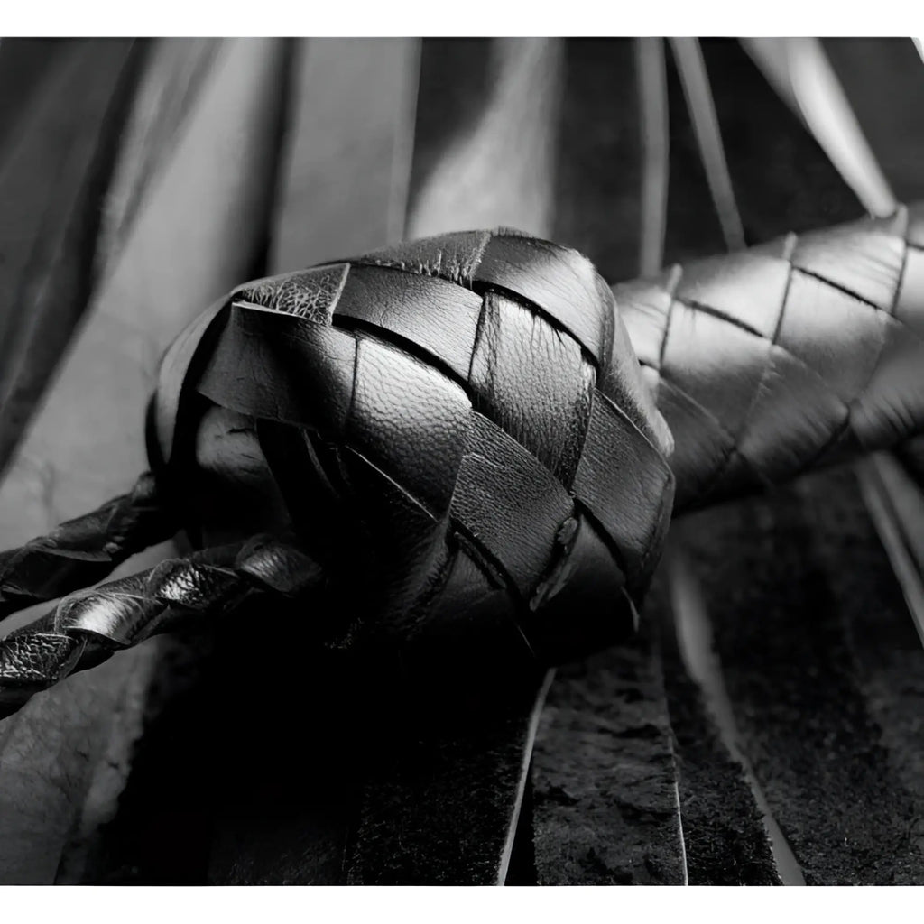 Strict Leather Premium Soft Leather Flogger: A close-up of a black, hand-braided leather handle and dangling fringe.