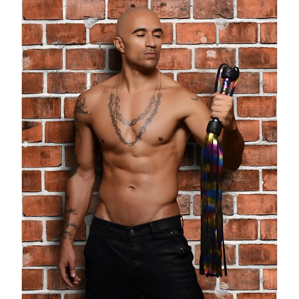 Strict Leather Rainbow Flogger: A shirtless man holding a metallic rainbow-colored multi-strand leather flogger.