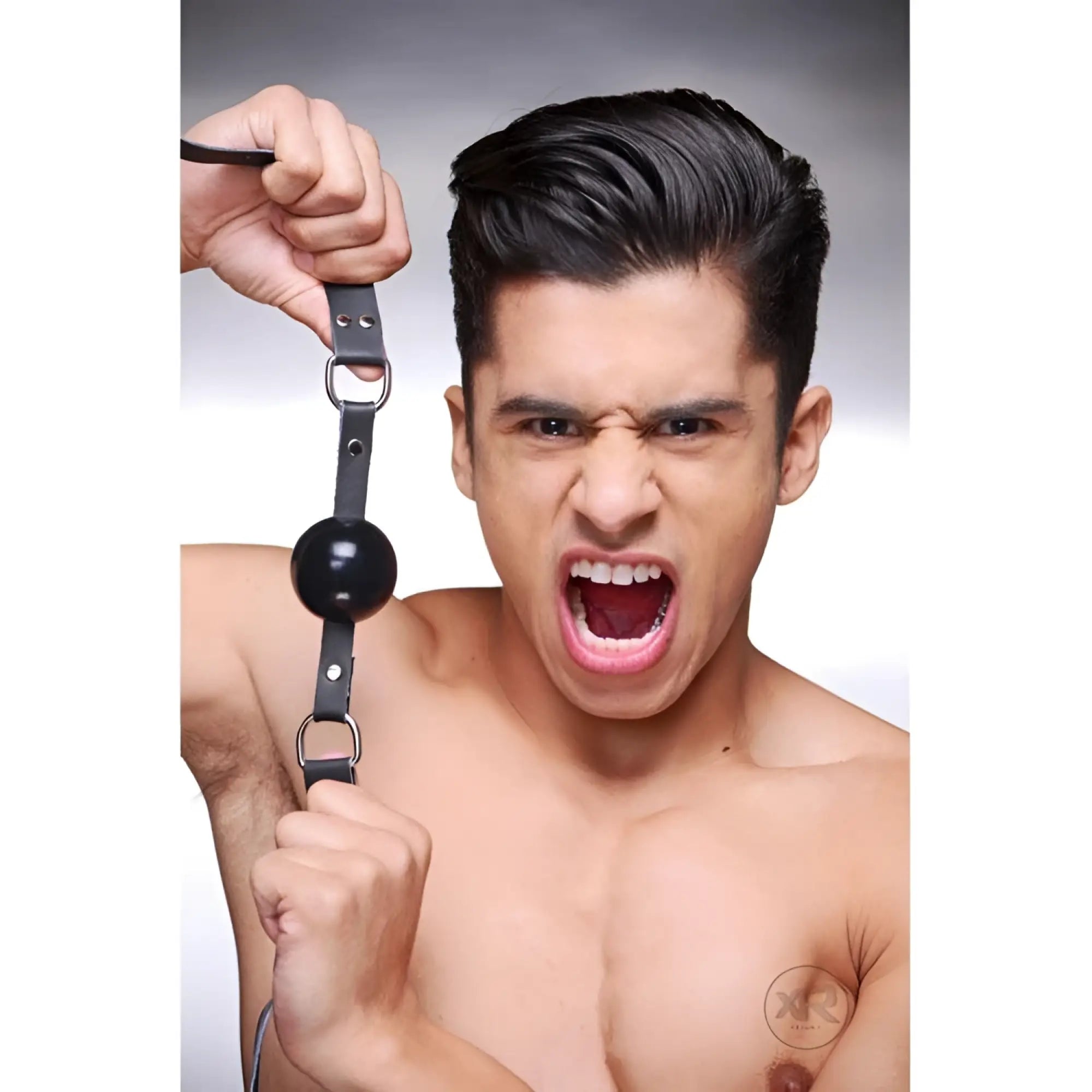 Strict Leather silicone ball gag with adjustable black leather straps, held by a shirtless man with an open mouth.
