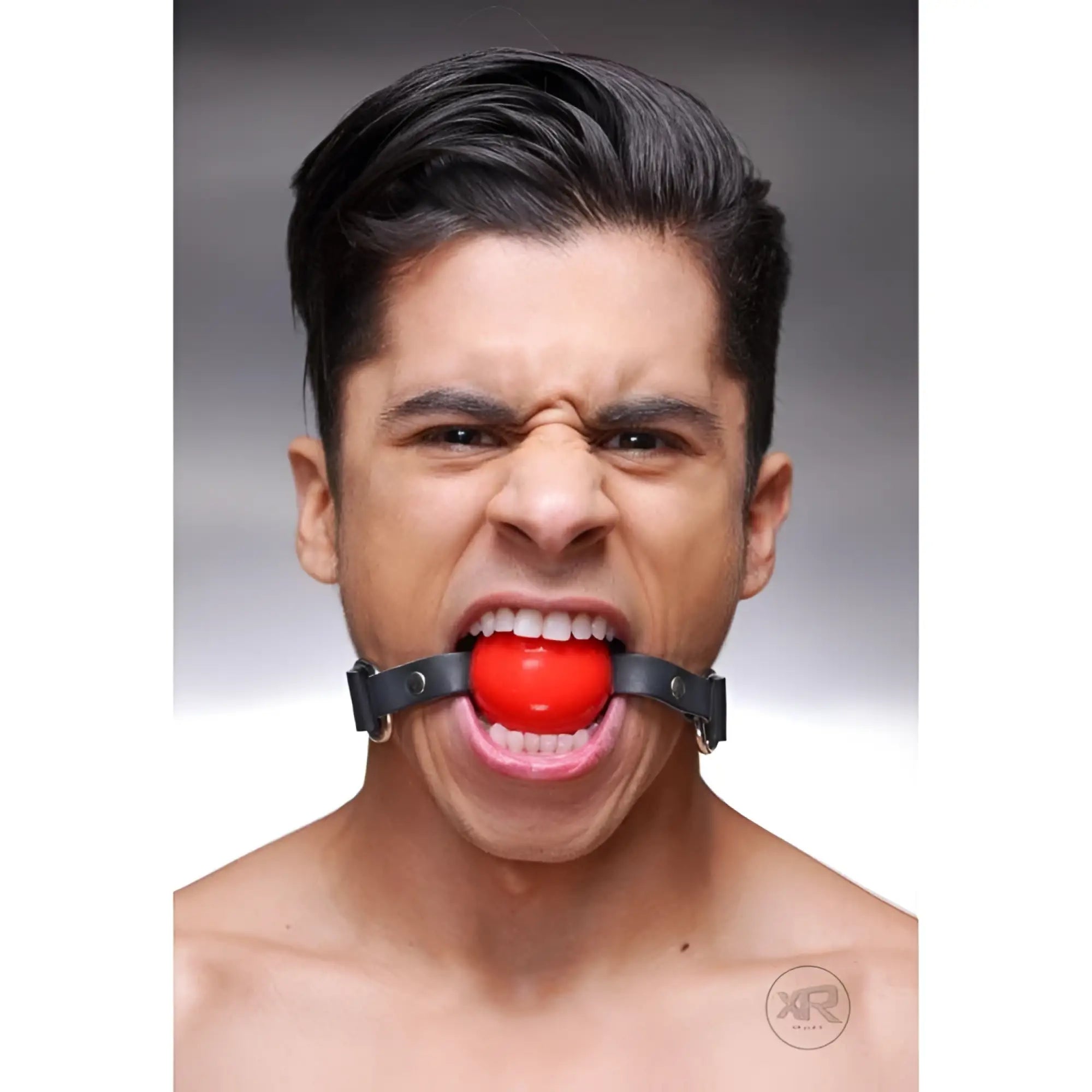 Strict Leather silicone ball gag with black leather straps worn by a man against a grey background.