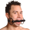 Strict Leather silicone bit gag with black rod and metal rings in a man's mouth against a white background.