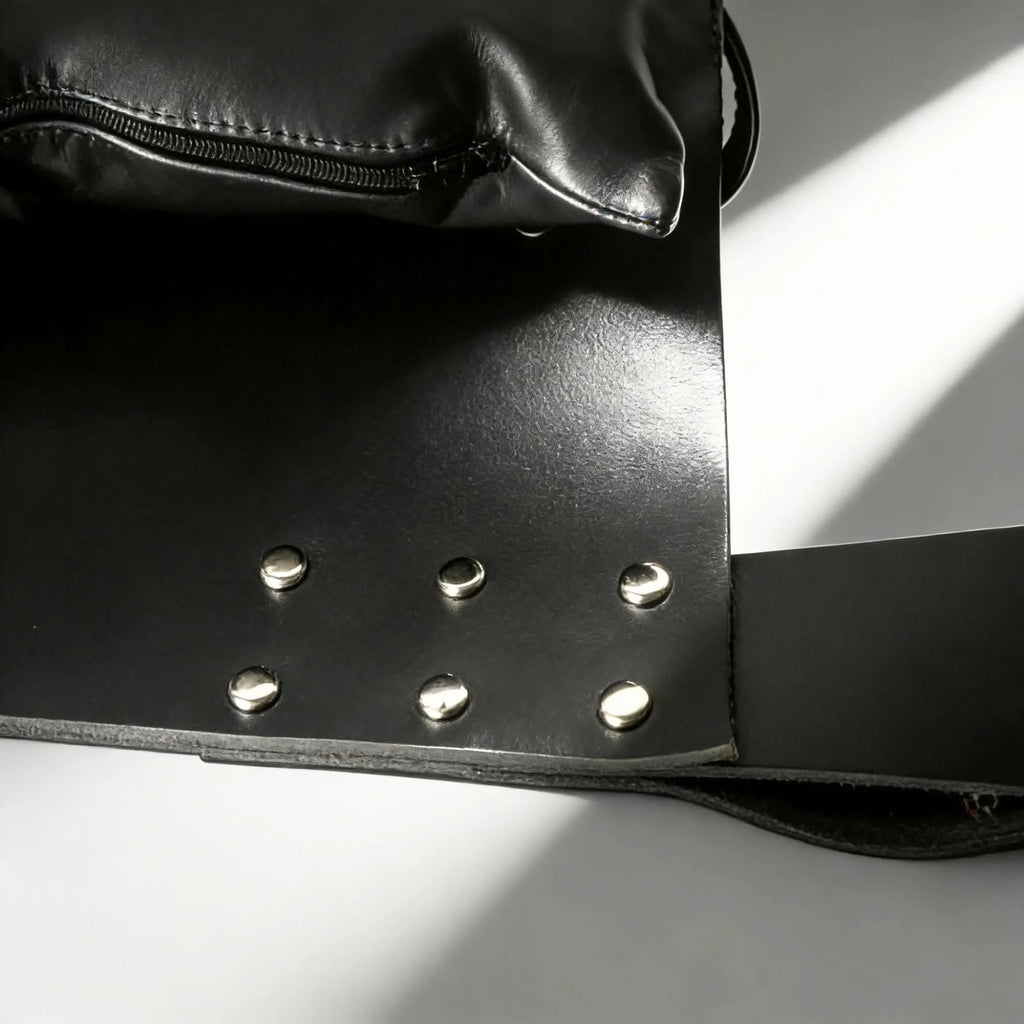 Strict Leather Sling with attached pillow, featuring black leather and silver metal studs in a minimalist, modern style.