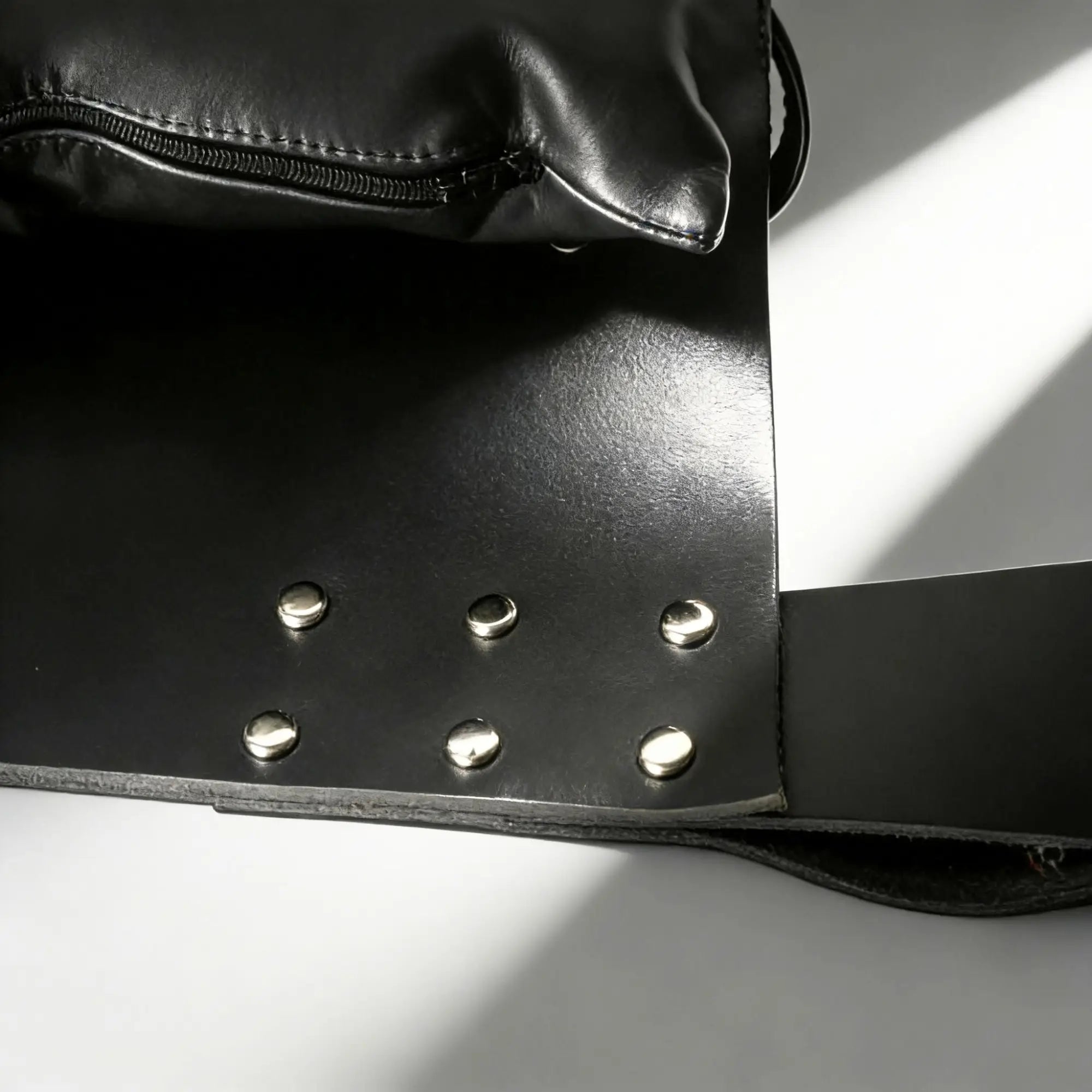 Strict Leather Sling with attached pillow, featuring black leather and silver metal studs in a minimalist, modern style.
