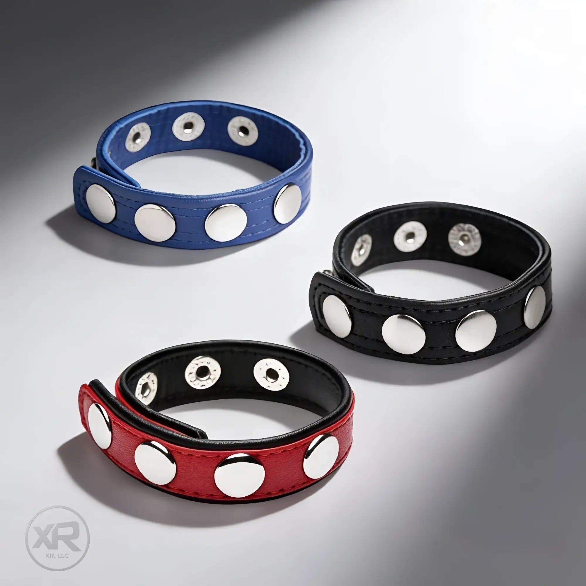 Three leather wristbands in red, blue, and black, each with multiple silver snap closures.