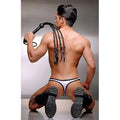 A man in a white thong and black boots holds a black Strict Leather Tigress whip with braided tails over his shoulder.