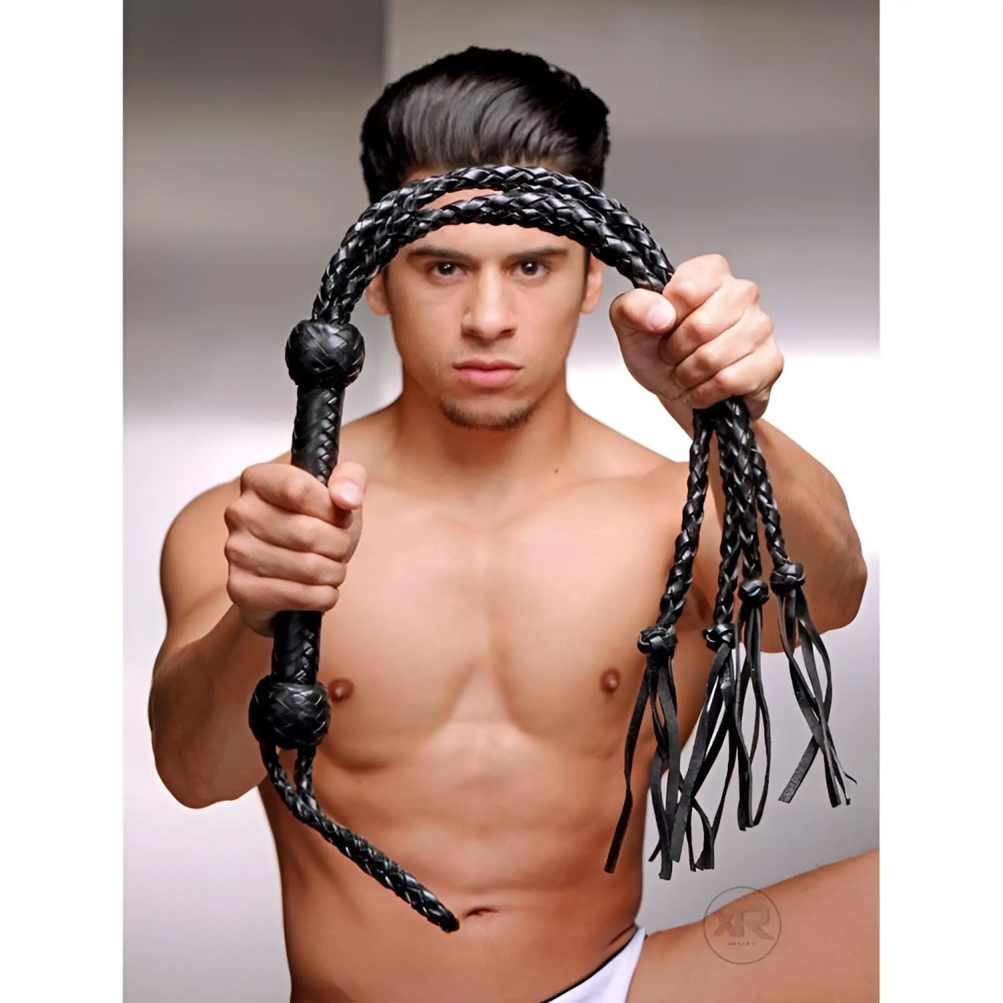 Strict Leather Tigress Whip: A shirtless man holding a braided black leather multi-tail flogger.