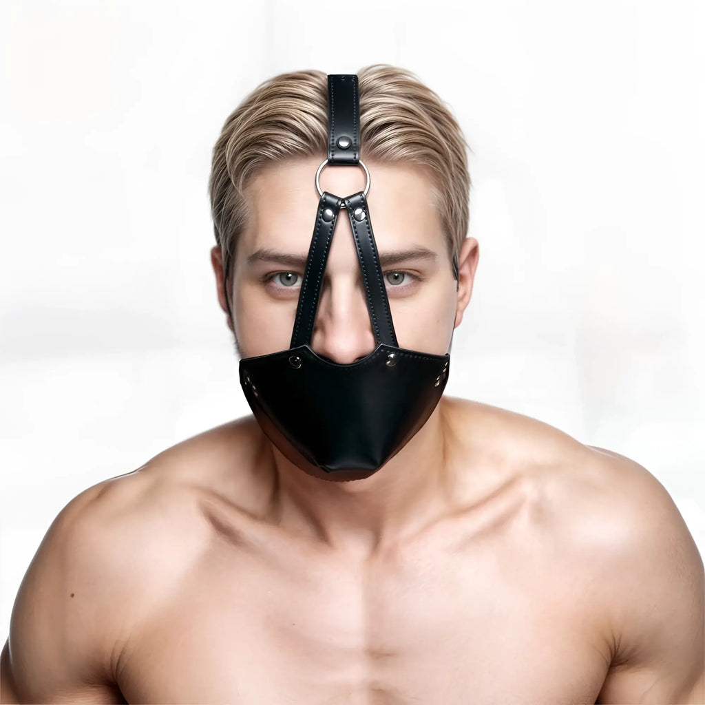 A shirtless man wears a black leather Strict Muzzle Harness with a concealed ball gag against a white background.