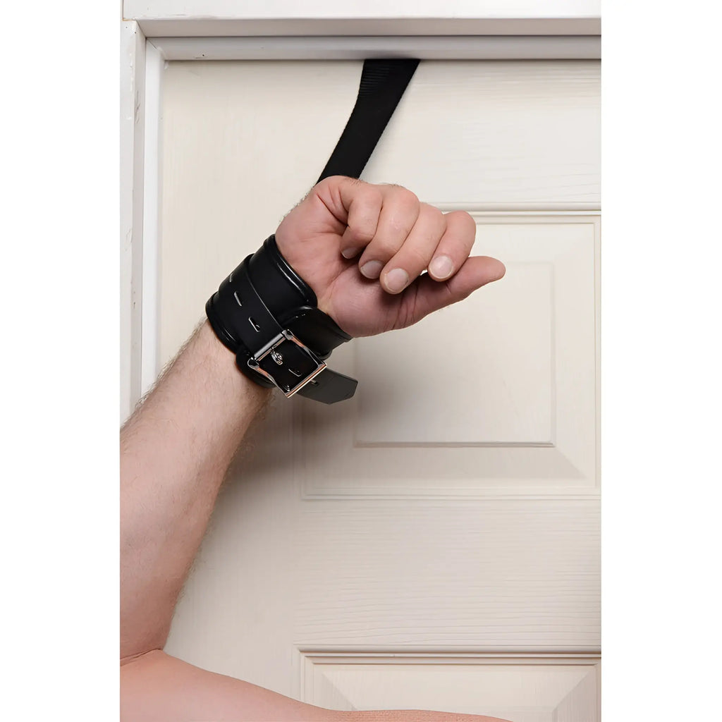 Strict Over the Door Restraint: A black padded wrist cuff with a silver buckle anchored over a door by a nylon strap.