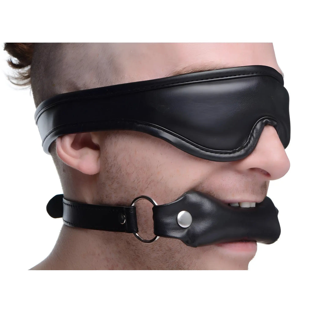 Strict Padded Blindfold and Gag Set: Black leather-style, padded blindfold and matching mouth gag on a person's face.