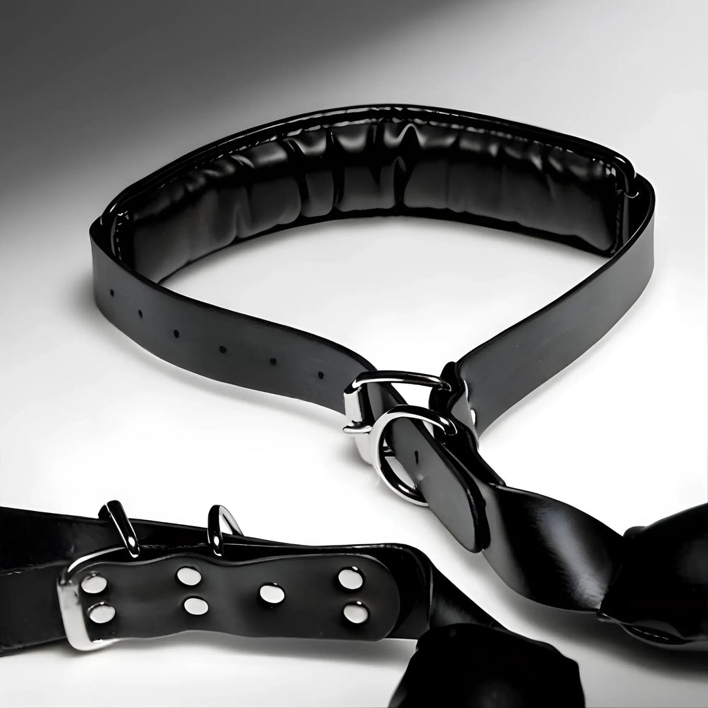 Strict Padded Thigh Sling with Wrist Cuffs: A black, glossy padded restraint set with silver-toned buckles and D-rings.