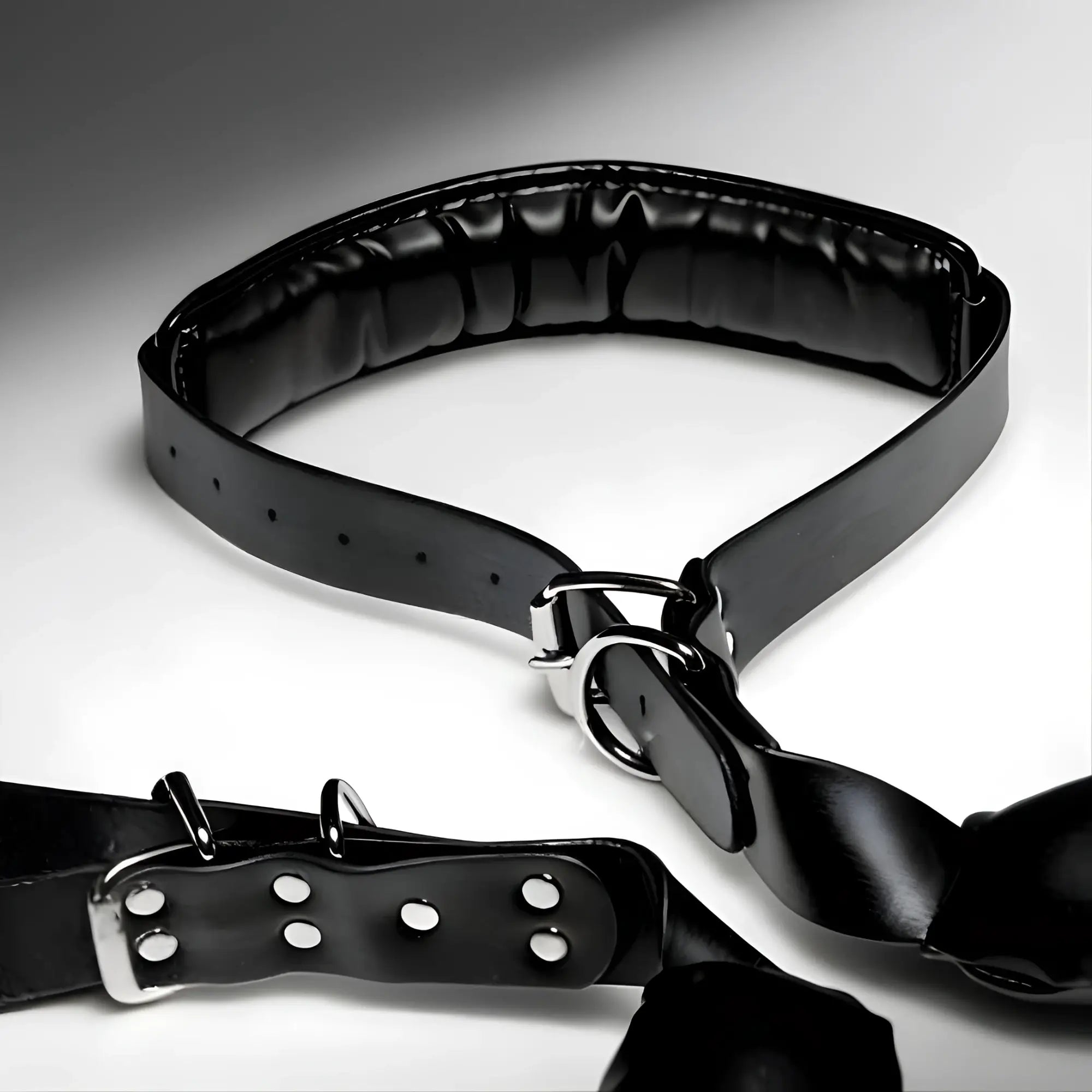 Strict Padded Thigh Sling with Wrist Cuffs: A black, glossy padded restraint set with silver-toned buckles and D-rings.