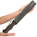 A hand holds a Strict Scottish Tawse, a black leather paddle with a brown embossed handle and a hanging cord.