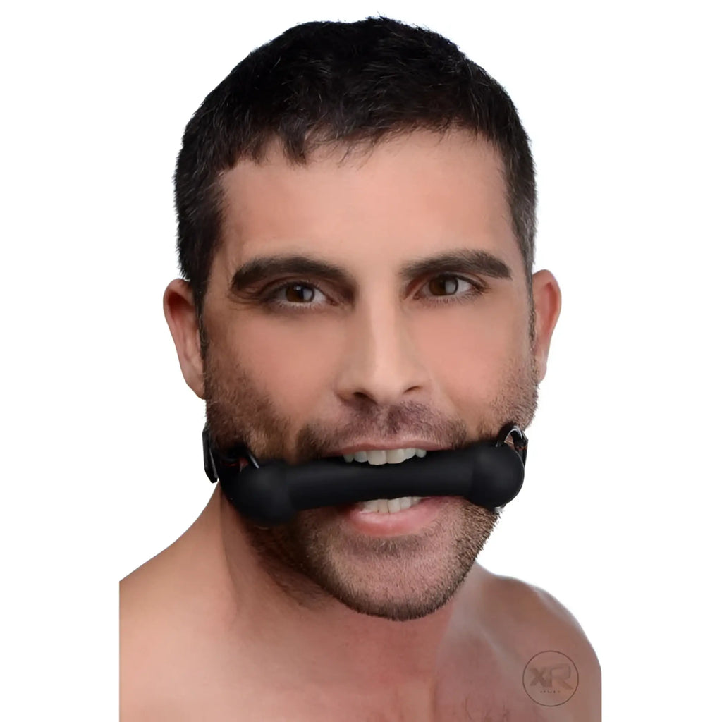A man wearing a black, cylindrical Strict Silicone Bit Gag held horizontally between his teeth.