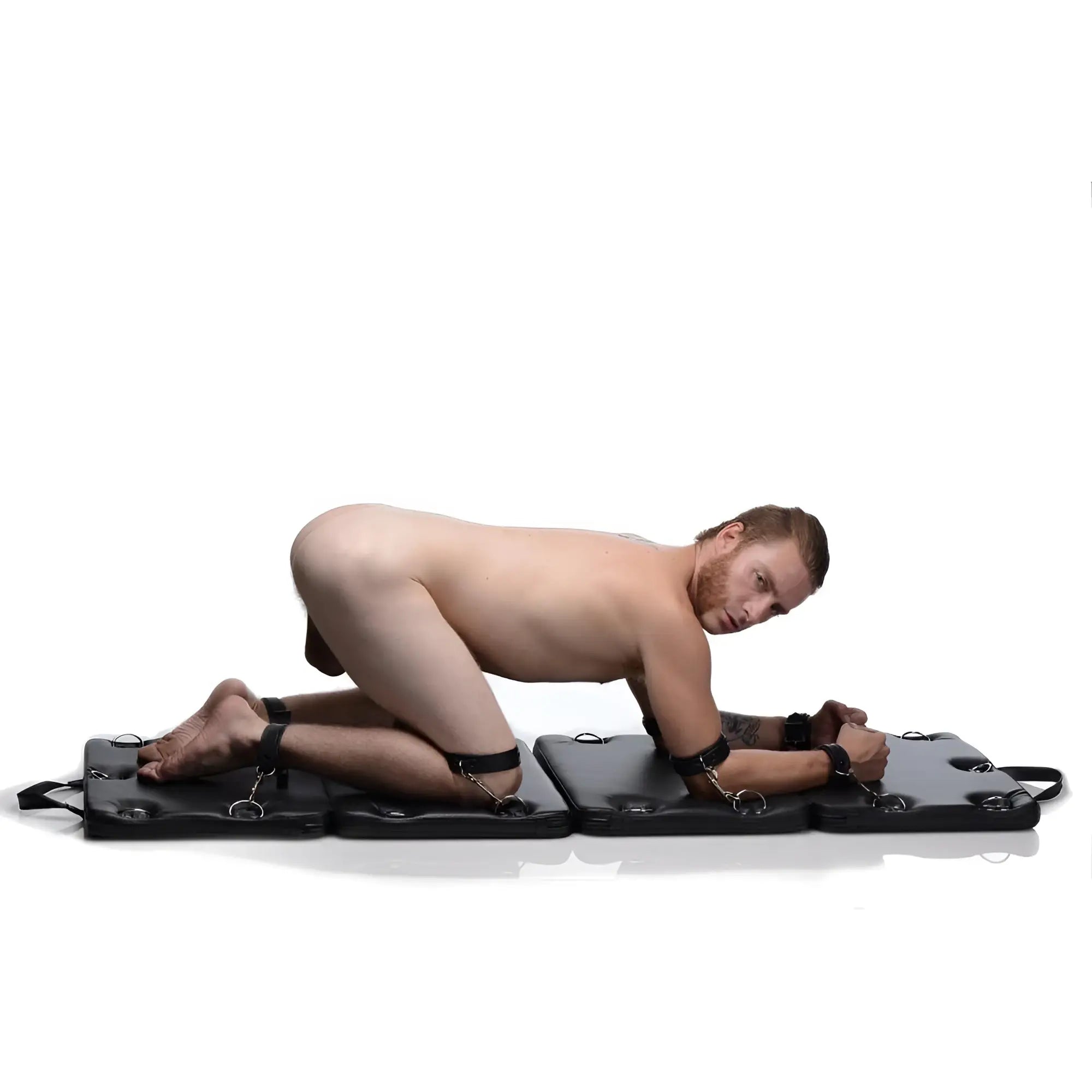 Strict XL Bondage Board: A man on hands and knees, limbs secured to a foldable, black padded mat with metal rings.