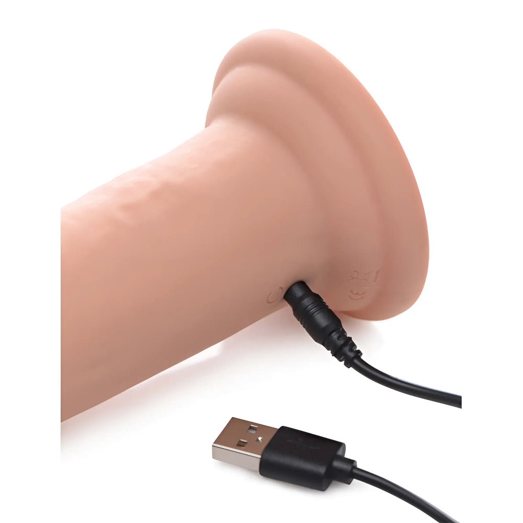 Swell 7X silicone dildo in skin tone, showing the charging port with a connected black USB charging cable.