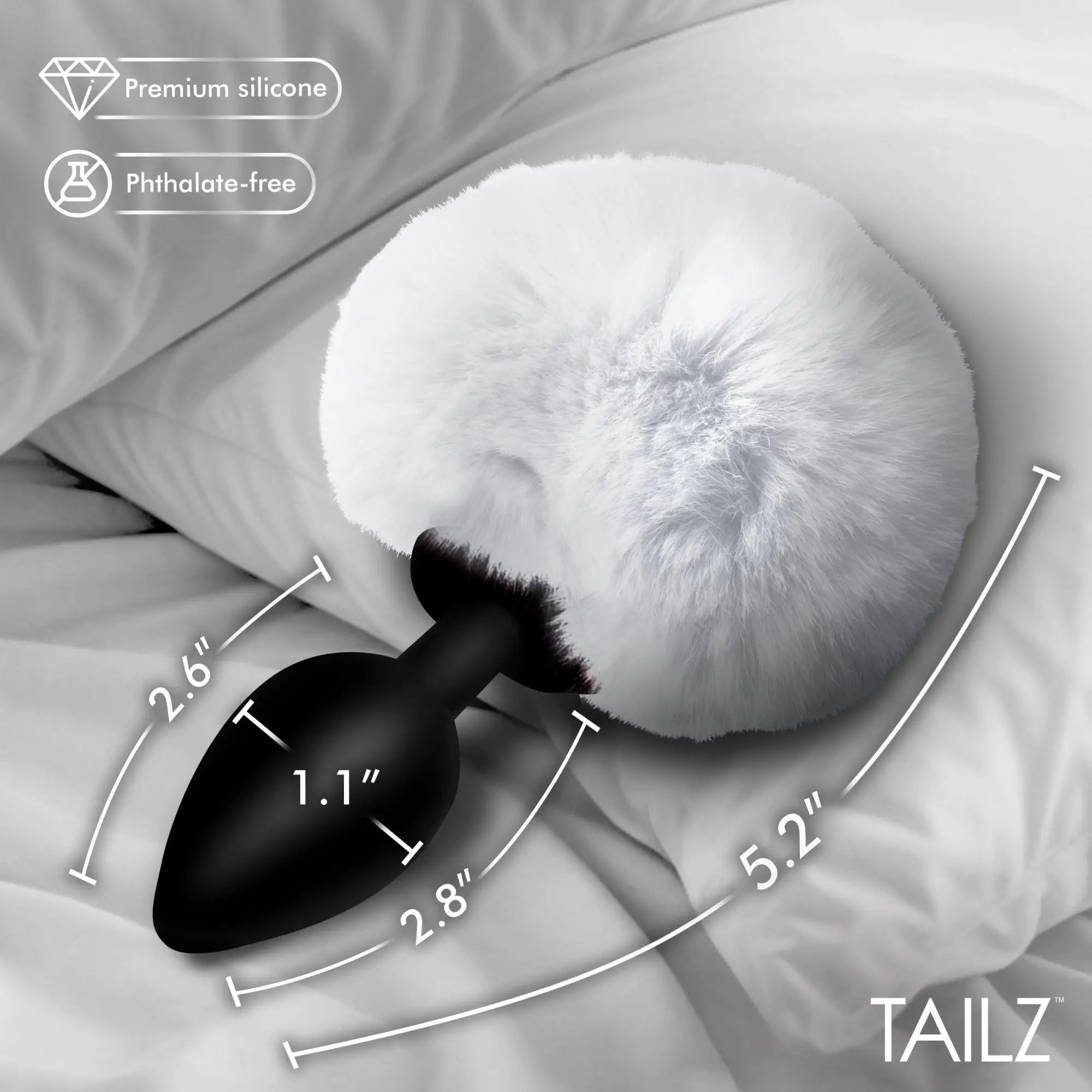 Tailz Fluffy Bunny Tail black silicone plug with white faux fur, featuring measurement lines on a white bedding backdrop.