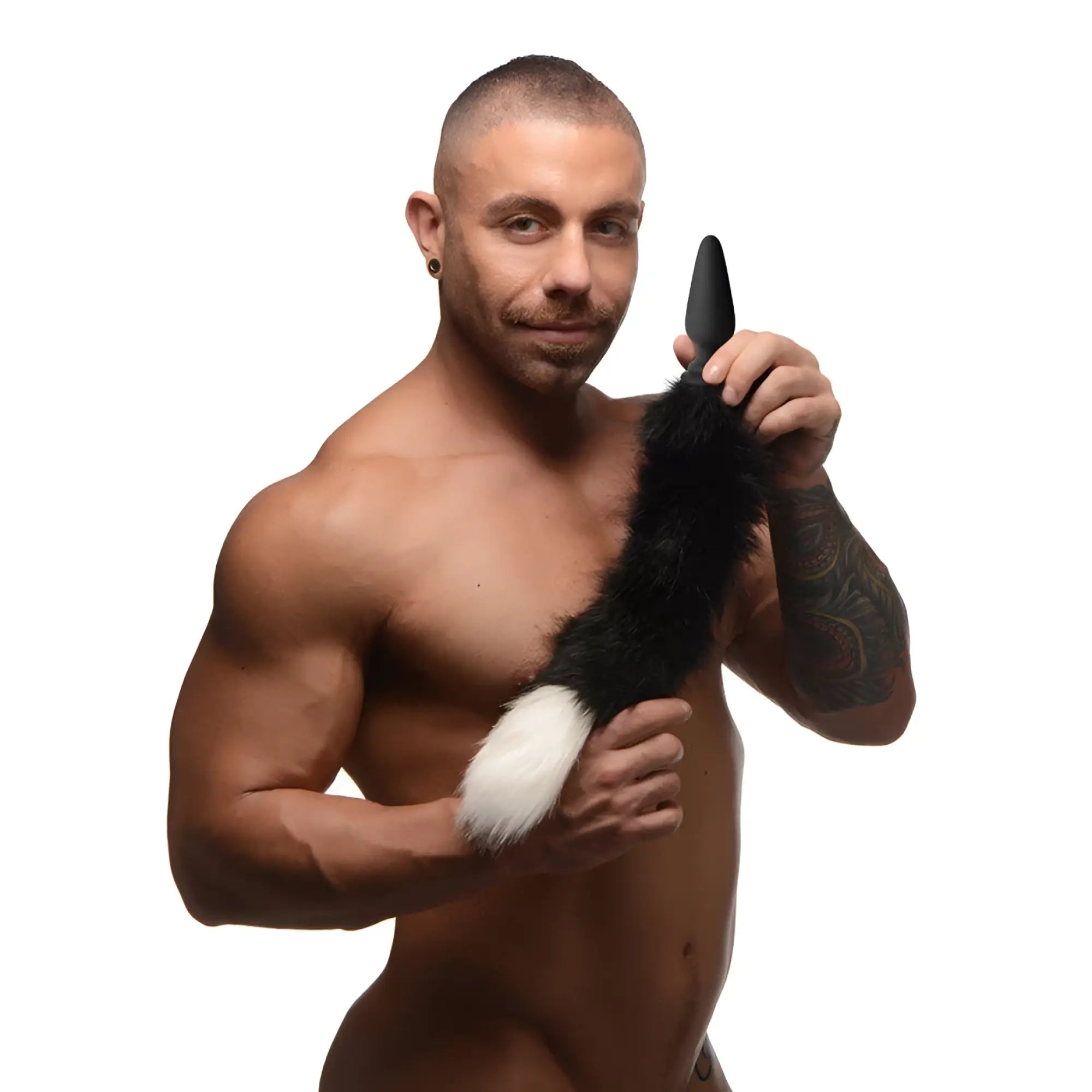 A shirtless man holding a black Tailz anal plug with a black and white faux fur fox tail attached.