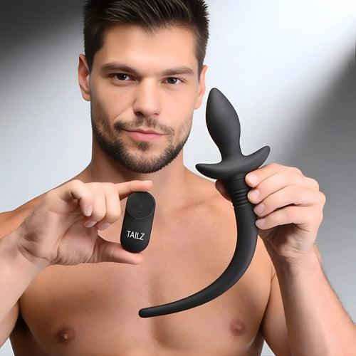 A man holding a black Tailz remote control wagging and vibrating puppy tail anal plug with a matching remote.