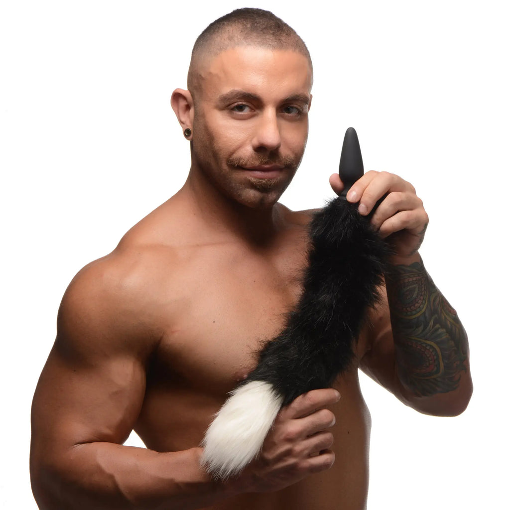 A man holds a black Tailz small anal plug attached to a black-and-white fluffy faux-fur fox tail.