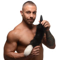 A man holds a black Tailz small anal plug attached to a black-and-white fluffy faux-fur fox tail.