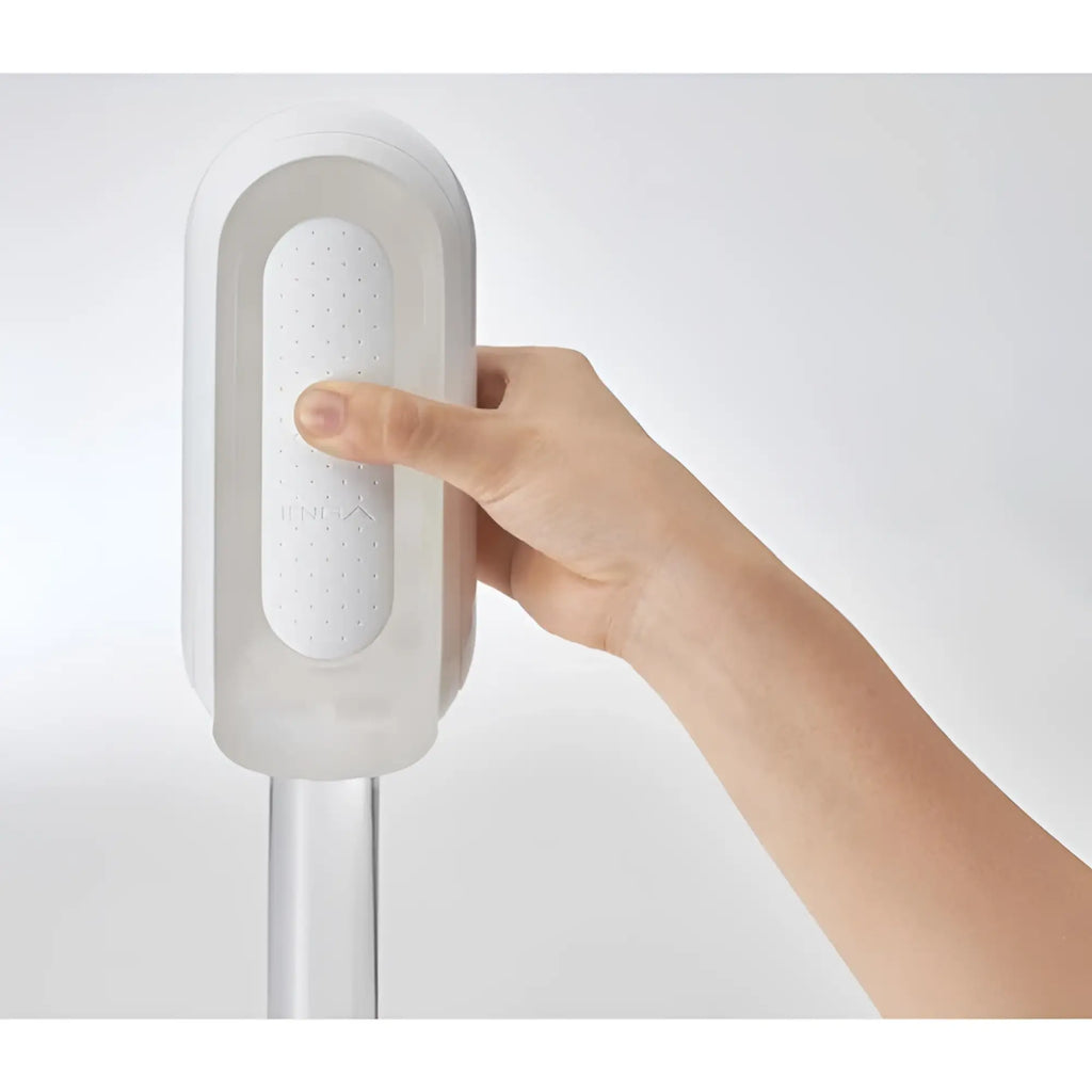 A hand holds a white Tenga Flip 0 (Zero) device featuring a sleek, minimalist design against a plain background.