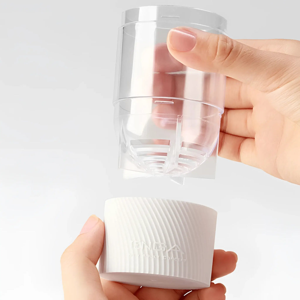 Hands hold the Tenga Spinner 06 Brick stroker, showing its clear internal sleeve and white textured outer shell.