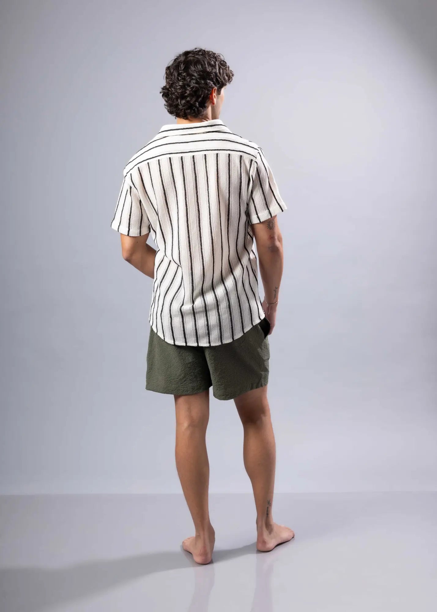 A man wearing a black and white striped texture knit short-sleeved button-up shirt for casual wear