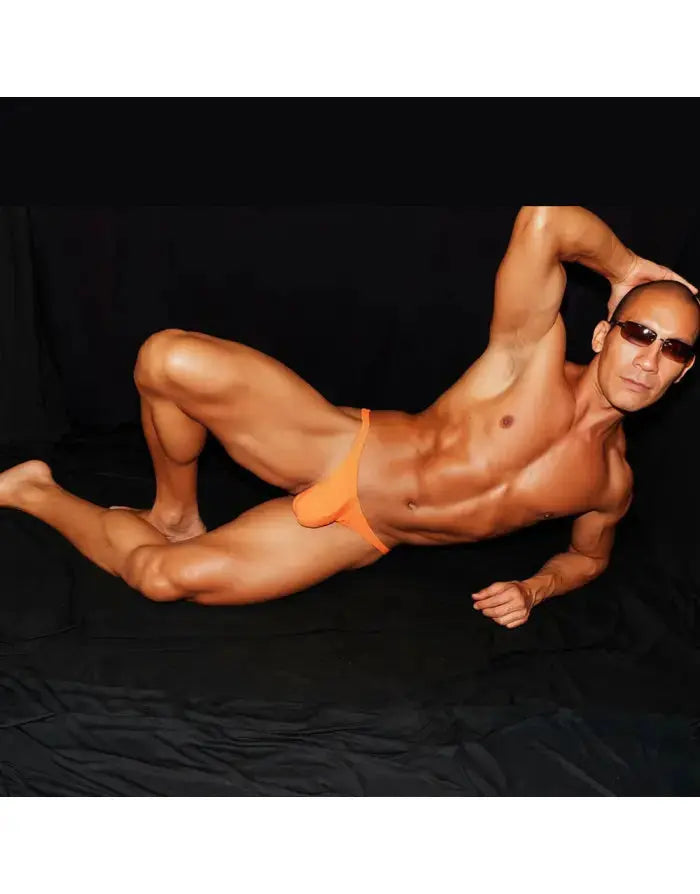 Model wearing Arroyman orange thong underwear featuring a snug fit and minimal coverage posed against a dark background.
