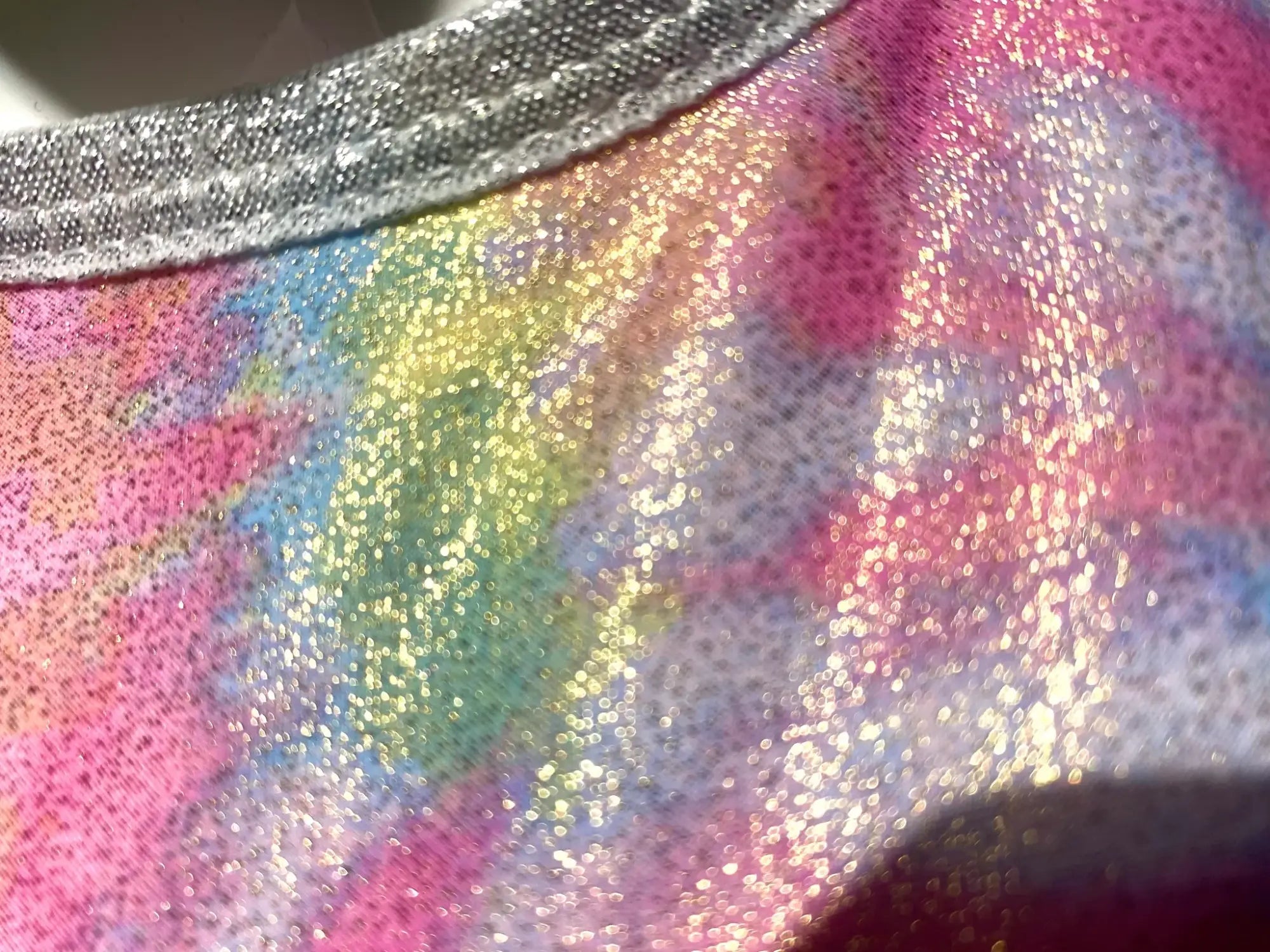 A shimmering iridescent tie dye crop top with a rainbow gradient pattern and silver glitter trim