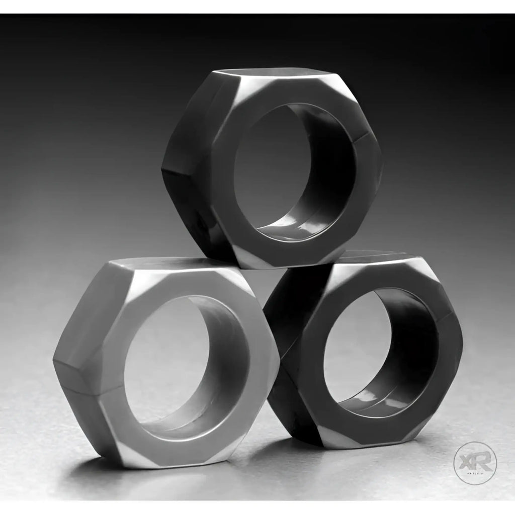 Tom of Finland 3 Piece Cock Nuts: A stack of three smooth, matte black hexagonal metal rings on a grey background.