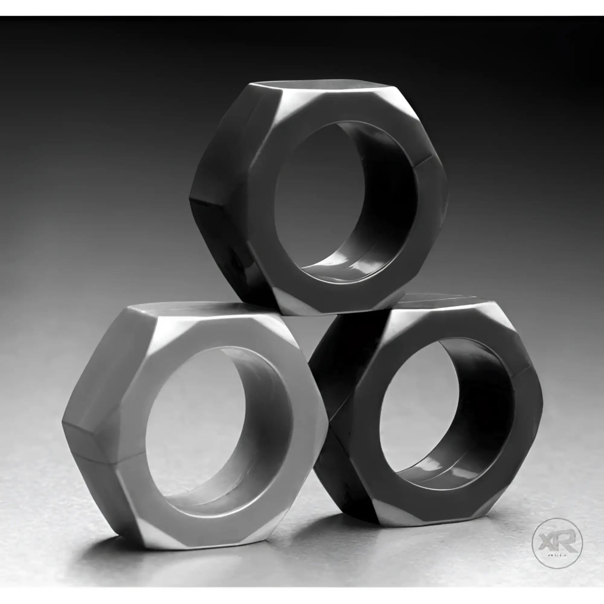 Tom of Finland 3 Piece Cock Nuts: A stack of three smooth, matte black hexagonal metal rings on a grey background.