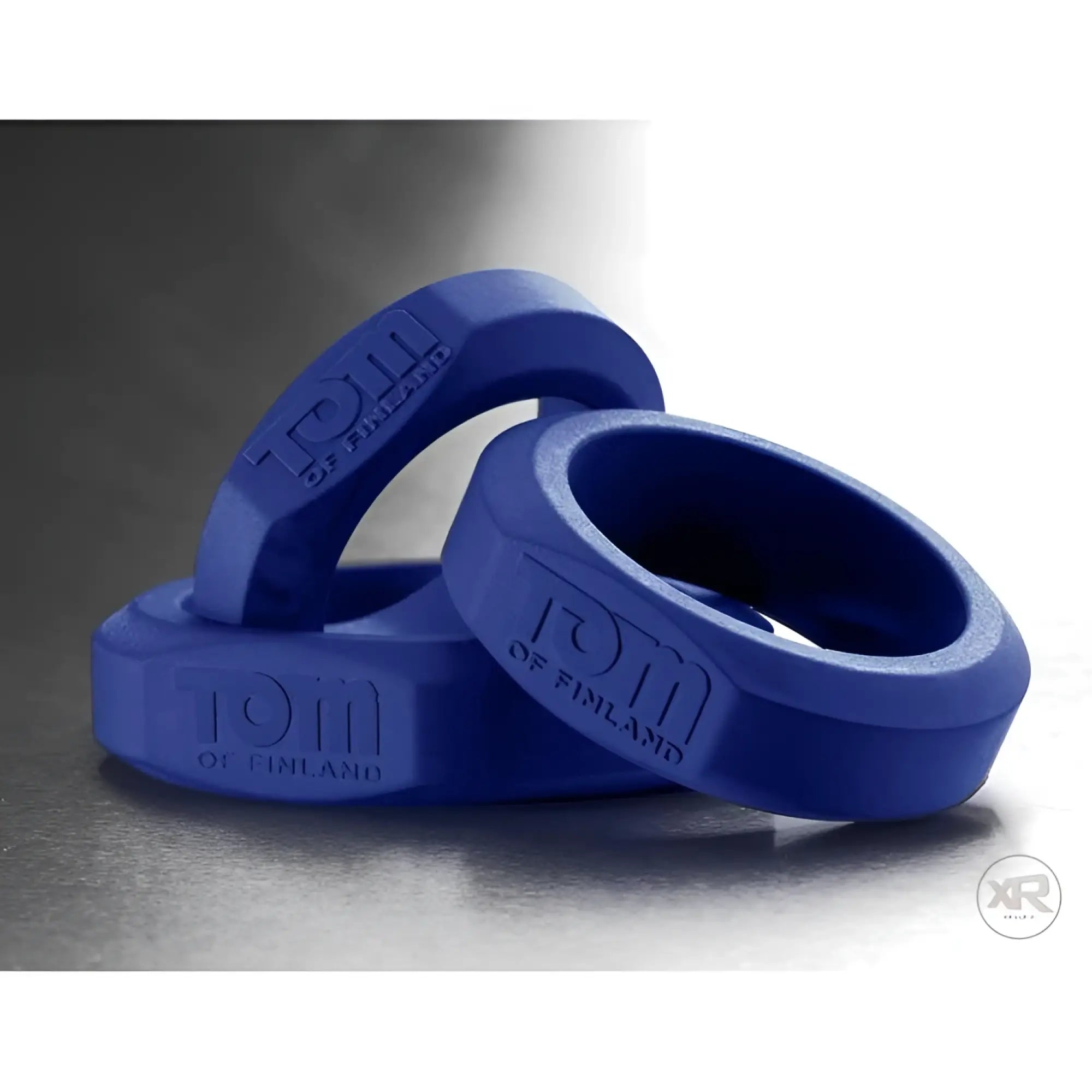 Three blue silicone Tom of Finland cock rings stacked on a grey surface, each embossed with the brand logo.