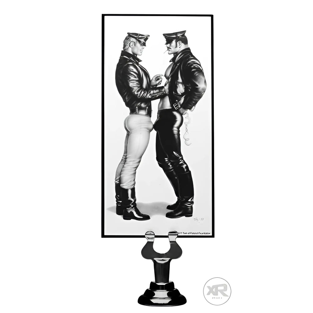 Black and white framed artwork of two men in leather attire displayed on black metal stand for tom of finland